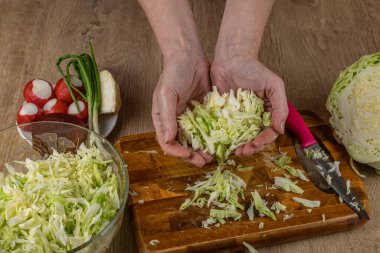 Dişi bir sebze salatası hazırlıyor. Yakın plan kadın elleri, doğranmış beyaz lahanayı sebze salatasıyla dolu bir kaseye koyuyor. Taze vejetaryen sağlıklı salata pişirme kavramı..