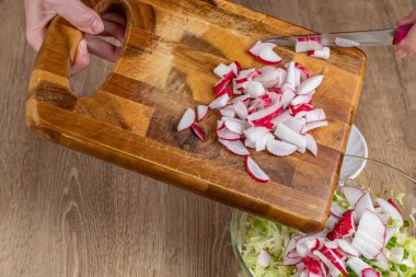 Aşçı ahşap bir kesme tahtasından kesilmiş kırmızı bir turpu sebze salatası kasesine koyar. Ev mutfağında taze sebze salatası pişiriyorum. Doğal gıda kavramı sağlık için yararlıdır..