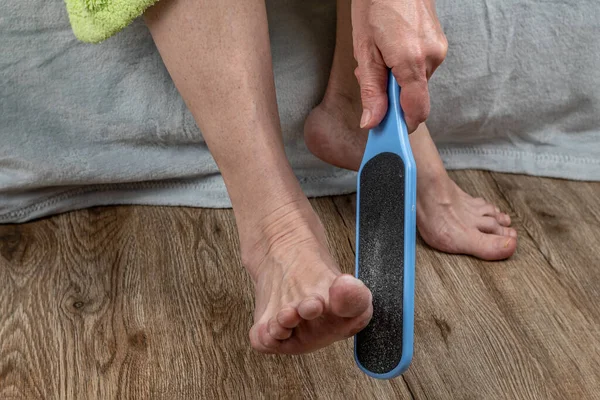 The girl cleans the heels of the feet with a grater for the skin of the feet. Foot care at home. Removal of corns on the heels of female feet. Pedicure at home. Leg skin care concept.