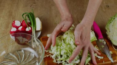 Kadın elleriyle doğranmış beyaz lahanayı alıyor ve lahana kabını bir kase salataya koyuyor. Bir ev hanımı taze sebze salatası hazırlar. Taze sebzelerden salata pişirme kavramı.