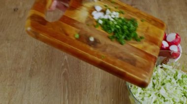 Dişi taze sebze salatası hazırlıyor. Salata kasesine doğranmış yeşil soğan dökülen ahşap bir kesme tahtasının yakın çekimi. Sağlıklı bir yaşam tarzı. Sağlıklı çiğ vejetaryen yemeği kavramı..
