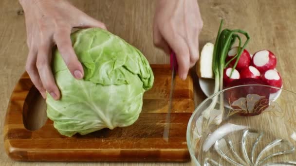 主婦は野菜サラダを作るために白菜を薄く切っている 台所のテーブルの上に木製のまな板に白いキャベツを切る女性の手のクローズアップ ベジタリアンとローフードのコンセプト — ストック動画