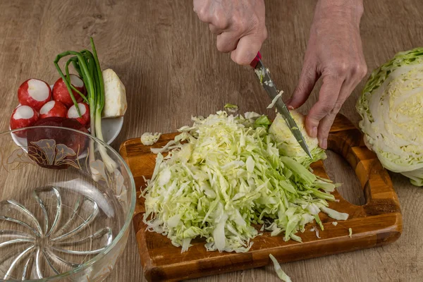A woman cuts vegetables on a wooden cutting board for making vegetable salad from fresh raw vegetables cabbage, radish, green onion, red beet, celery root. Raw food and veganism.