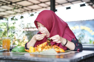 A woman in a hijab is eating crab seafood