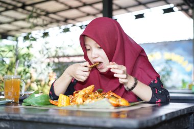 A woman in a hijab is eating crab seafood
