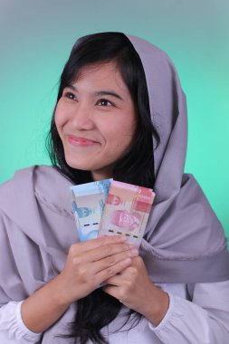A girl holding Indonesian currency, 100,000 and 50,000 rupiah banknotes with cyan background