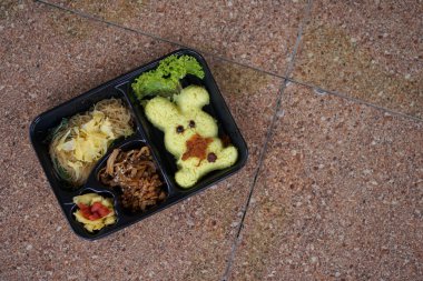 Yanında sebze, erişte ve tempeh tabakları olan oyuncak bebek şeklinde sarı pirinç.