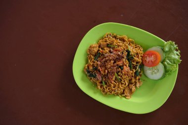 Endonezyalı Mie Goreng yeşil bir tabakta sebze, yumurta ve kızarmış arpacık soğanı ile