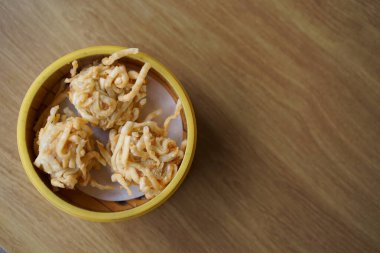 Tahta bir masada, bambu buharlı sepetin içinde üç altın sarısı kızarmış hamur köftesi. Dim Sum kavramı.