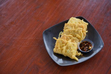 Baharatlı soslu kızarmış tempeh, ahşap masada servis edilen siyah tabakta servis ediliyor. 