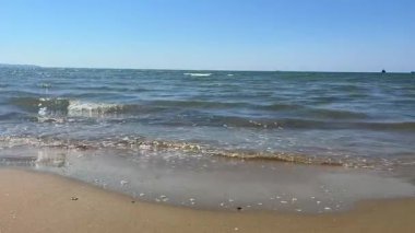 Mavi deniz ve ıslak kumun sahil şeridinde buluşmasını gösteren açık ve parlak bir video. Tatil ve rahatlama temaları için mükemmel..