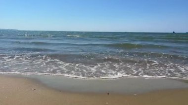 Kıyı şeridi boyunca uzanan desenli dalgaların yakın görüntüsü tekrar eden su akışını ve dokulu kumlu plajı vurguluyor..