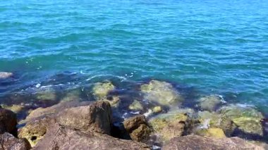 Sakin okyanus suları güzel mavi-yeşil renklerde geniş kıyı şeridi taşlarını sarar ve doğal temalar için mükemmel sakin bir sahil manzarası yaratır..
