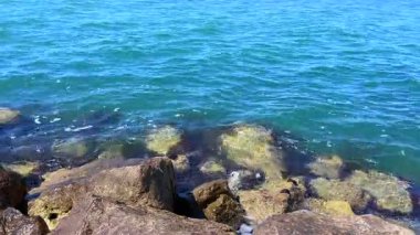 Parlak güneş ışığı, kristal berrak bir denizde hafif dalgalanmaları yansıtır. Batık kayaları ve kıyı şeridinin doğal dokusunu ortaya çıkarır..