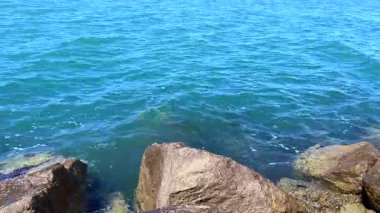 Kristal berrak deniz suyu, yuvarlak kıyı kaya kütlelerinin üzerinde yavaşça süzülerek rahatlatıcı ve meditasyon yapan bir okyanus manzarası yaratır..