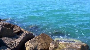 Parlak bir gökyüzünün altında sakin ve engin bir deniz ufku, pürüzsüz okyanus dalgaları kayalık bir kıyıya doğru yuvarlanıyor. Huzur ve seyahat odaklı görseller için ideal.