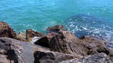 Yumuşak mavi dalgalar kahverengi kıyı şeridi üzerinde hareket eder. Kayalar, bu sakin ve detaylı deniz görüntülerinde ışığı ve hareketi yansıtır..