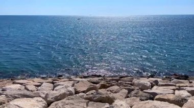 Sahilde taşlarla dolu denizi ve yukarıda güzel bir gökyüzünü gösteren manzaralı bir video. Huzurlu manzara seyahat, doğa ve kıyı temalı projeler için mükemmeldir..