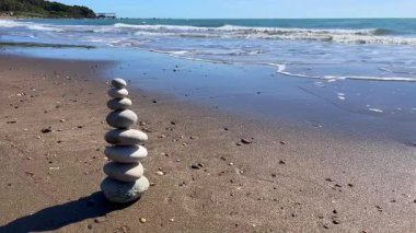 Açık mavi gökyüzü ve okyanusla kumsalda taş yığını
