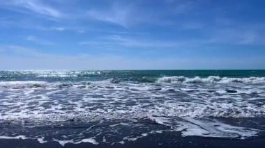 Okyanus dalgaları açık mavi gökyüzü ile sahile çarpıyor.