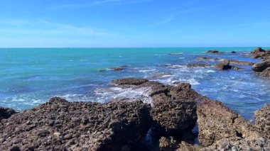 Mavi gökyüzünün altında okyanus dalgaları olan kayalık kıyı şeridi