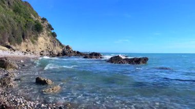 Çakılan dalgalar ve berrak mavi okyanus suyuyla kayalık sahil