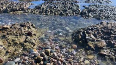 Sahil kayalarını gösteren sakin bir sahne kristal berrak su ve yumuşak dalgalarla çevrili, berrak mavi gökyüzünün altında..