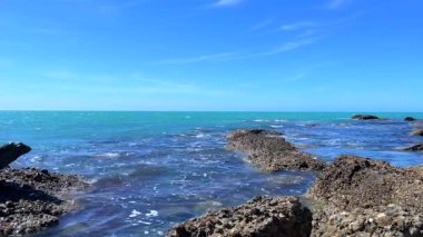 Bu video, okyanus dalgaları akarken kıyıdaki kayaları yakalıyor ve rahatlatıcı ve manzaralı bir plaj sahnesi yaratıyor. Berrak mavi su, kayalık sahil şeridiyle çok güzel zıtlaşıyor. Bu da burayı huzurlu plaj içeriği için ideal bir yer yapıyor..