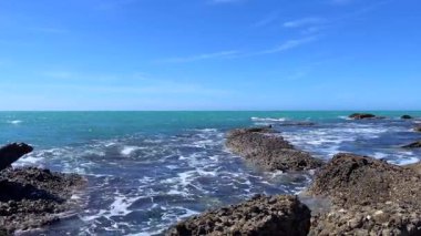 Bu video, kıyı şeridi boyunca kayalık oluşumlara çarpan okyanus dalgalarının hareketini yakalar. Sakin ve berrak su, güzel mavi gökyüzü ile birleşince, doğa ve rahatlama odaklı içerik için mükemmel huzurlu ve sakin bir atmosfer yaratır..