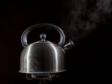 Gaz ocağındaki su ısıtıcısı. Karanlık bir arka planda ocakta çaydanlık, yakın plan..