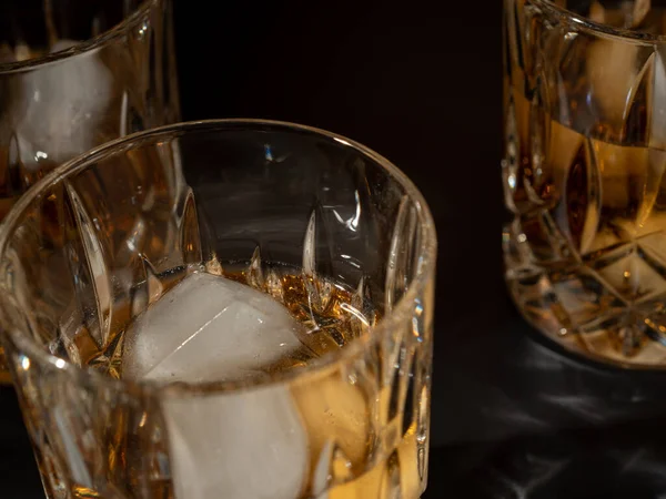 Whiskey, bourbon or cognac with ice cubes on a black background. Close-up.