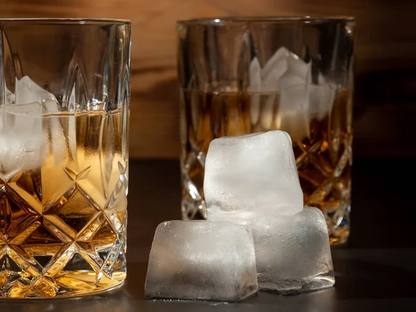 Whiskey, bourbon or cognac with ice cubes on black and wooden background. Close-up.