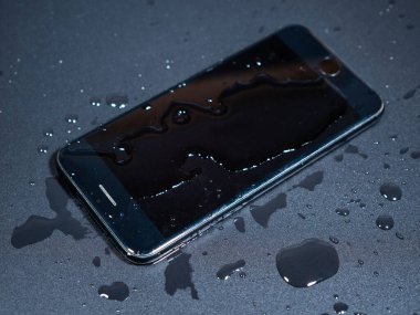 Siyah arka planda, suda eski bir telefonun yakın çekimi. Islak akıllı telefon..