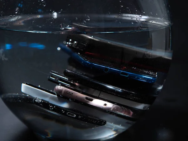 Close-up. Lots of old smartphones in the water on a black background. Wet smartphones.