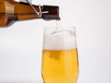 Taze bira şişeden bardağa dökülür. Beyaz arka planda bira. Yakın plan..