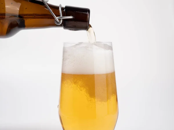 Fresh beer is poured from a bottle into a glass. Beer on a white background. Close-up.