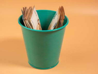 Turuncu arka plandaki çöp kutusunda para var. Avrolar çöpe. Para israfı kavramı. Yakın plan..