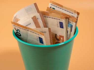 Turuncu arka plandaki çöp kutusunda para var. Avrolar çöpe. Para israfı kavramı. Yakın plan..