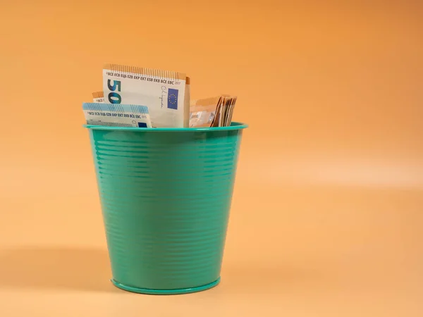 Money in the trash can on an orange background. Euros in the trash. Waste of money concept. Close-up.