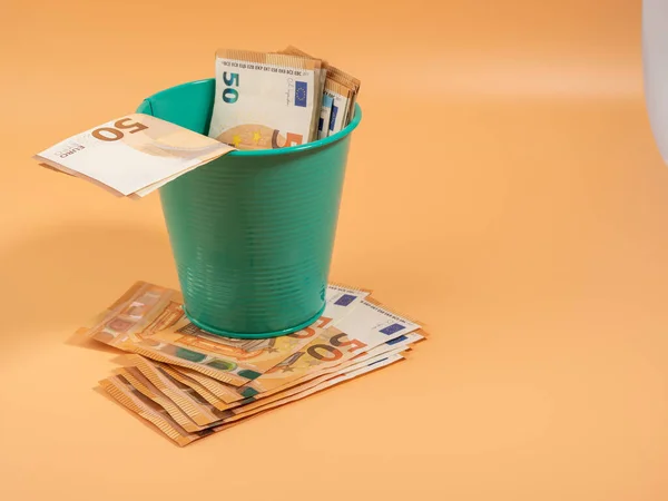 Money in the trash can on an orange background. Euros in the trash. Waste of money concept. Close-up.