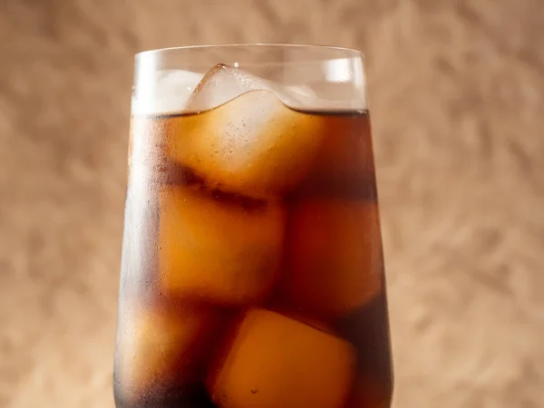 Cola with ice in a glass. Carbonated refreshing drink with ice. Cola bubbles. Macro photo.