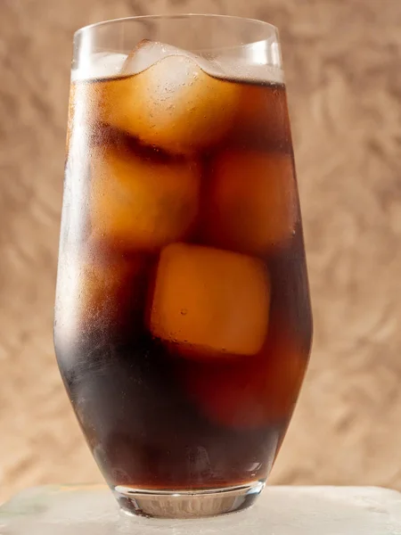 Cola with ice in a glass. Carbonated refreshing drink with ice. Cola bubbles. Macro photo.
