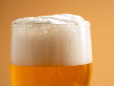 Köpüklü bir bardak bira. Turuncu arka planda bir kupa bira. Yakın plan..