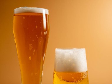 Köpüklü bir bardak bira. Turuncu arka planda bir kupa bira. Yakın plan..