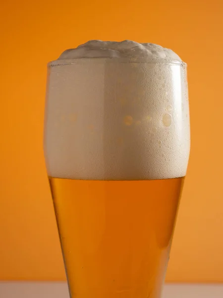 Glass of beer with foam. Mug of beer on an orange background. Close-up.