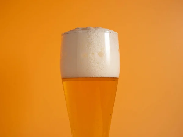 Glass of beer with foam. Mug of beer on an orange background. Close-up.