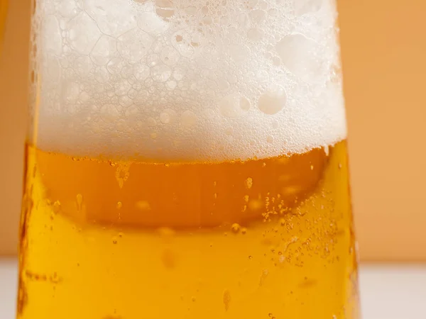 Glass of beer with foam. Mug of beer on an orange background. Close-up.