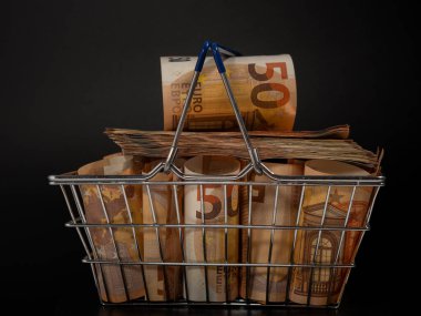 Shopping cart full of money. A shopping cart filled with euro banknotes. Shopping basket with money on a black background.