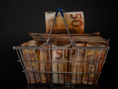 Shopping cart full of money. A shopping cart filled with euro banknotes. Shopping basket with money on a black background.