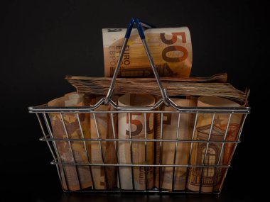 Shopping cart full of money. A shopping cart filled with euro banknotes. Shopping basket with money on a black background.
